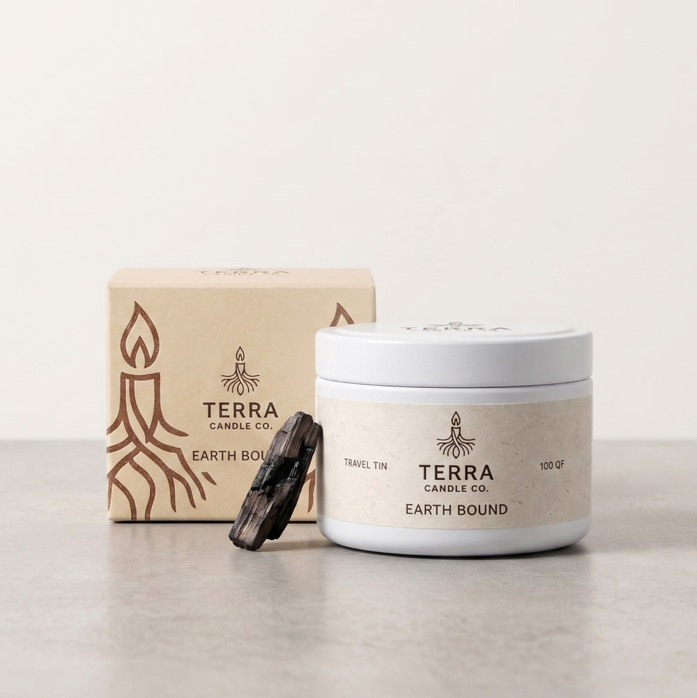 A Terra Candle Co. Earth Bound travel tin candle jar with its kraft paper packaging box and a small dark amber sachet, set against a neutral cream background.